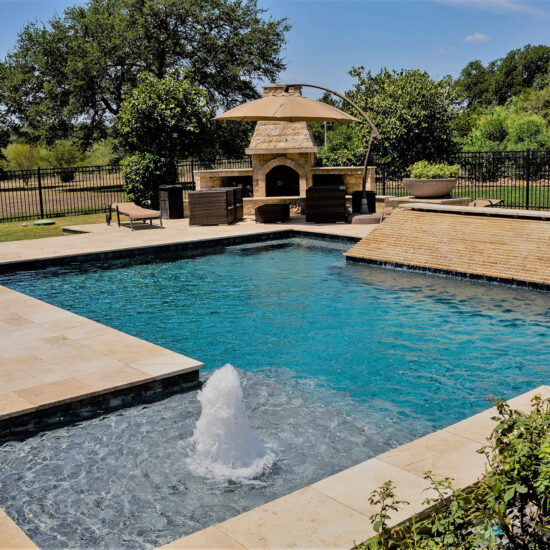 This modern geometric pool features an outdoor fireplace, sheer descent, and stunning water features.