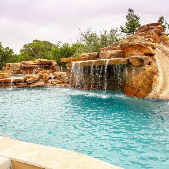 Custom freeform pool features a stunning lateral waterfall grotto and jump rock.